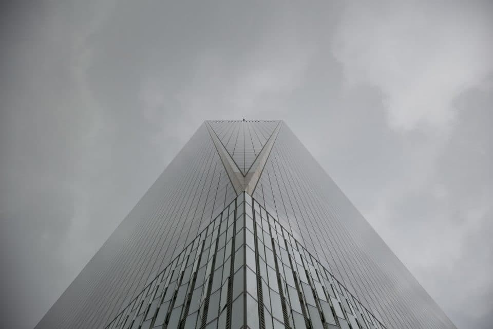 A tall office tower rising into low cloud, seen from street level.